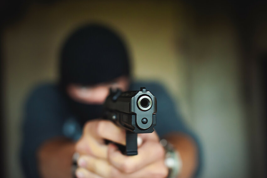 Athletic man in a balaclava, holds a pistol in his hand, is threatened with shooting, aiming