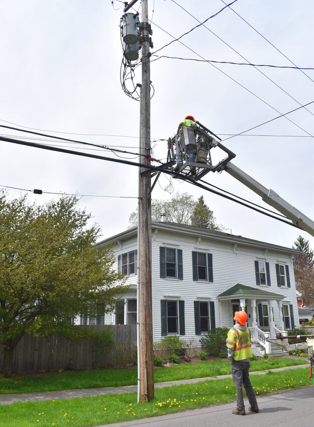 Sam Taylor, on the ground, observes Caleb Neiss, aerial line workers with Syracuse Utilities, install high-speed broadband lines Friday on Mill Street as part of Dryden Fiber.