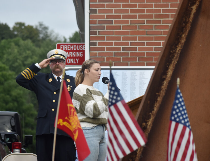 Homer Fire Department past chief John Riley salutes as Homer High School senior Mikayla Smith sings the national anthem at a memorial Monday evening in Homer marking the 22nd anniversary of the attacks of Sept. 11, 2001. The event was at the site of a piece of steel from the World Trade Center.