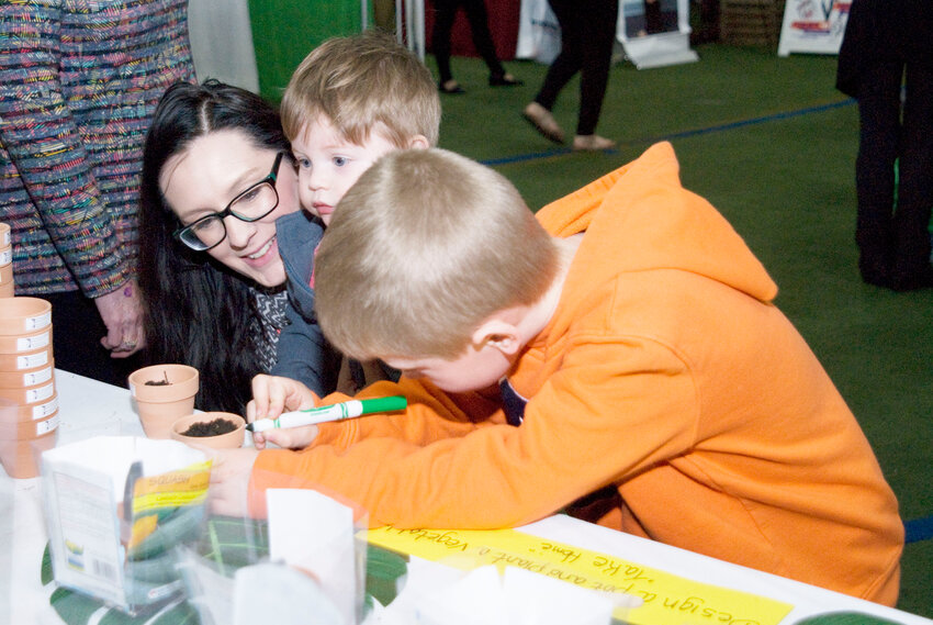 Samantha Pickert holds her 1-year-old son, Drew Pickert, while she watches her other son Kayden Jebbett, 6, draw on his flower pot at the Showcase in 2019. People were able to plat seeds in small pots at the Asthma and Allergy Associates booth during The Showcase returns April 5 at the J.M. McDonald Sports Complex in Cortlandville.