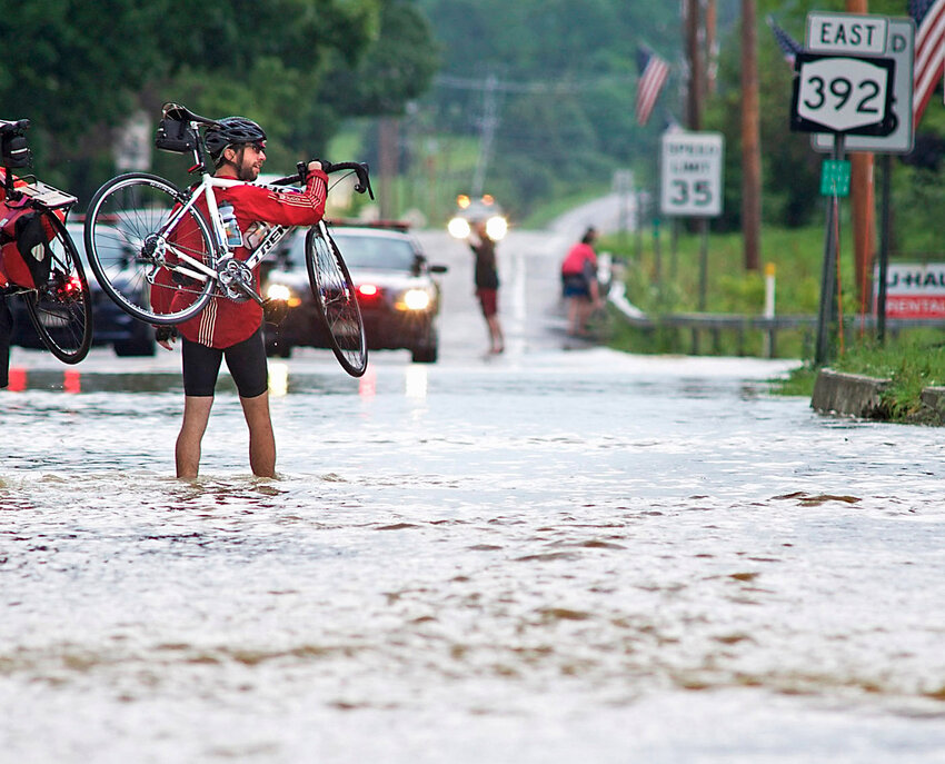 Matt Hollenbeck of Virgil walks his bike through floodwaters flowing through the center of Virgil in July 2017. The National Weather Service will train people to become weather spotters, to reduce hazards during events like this.