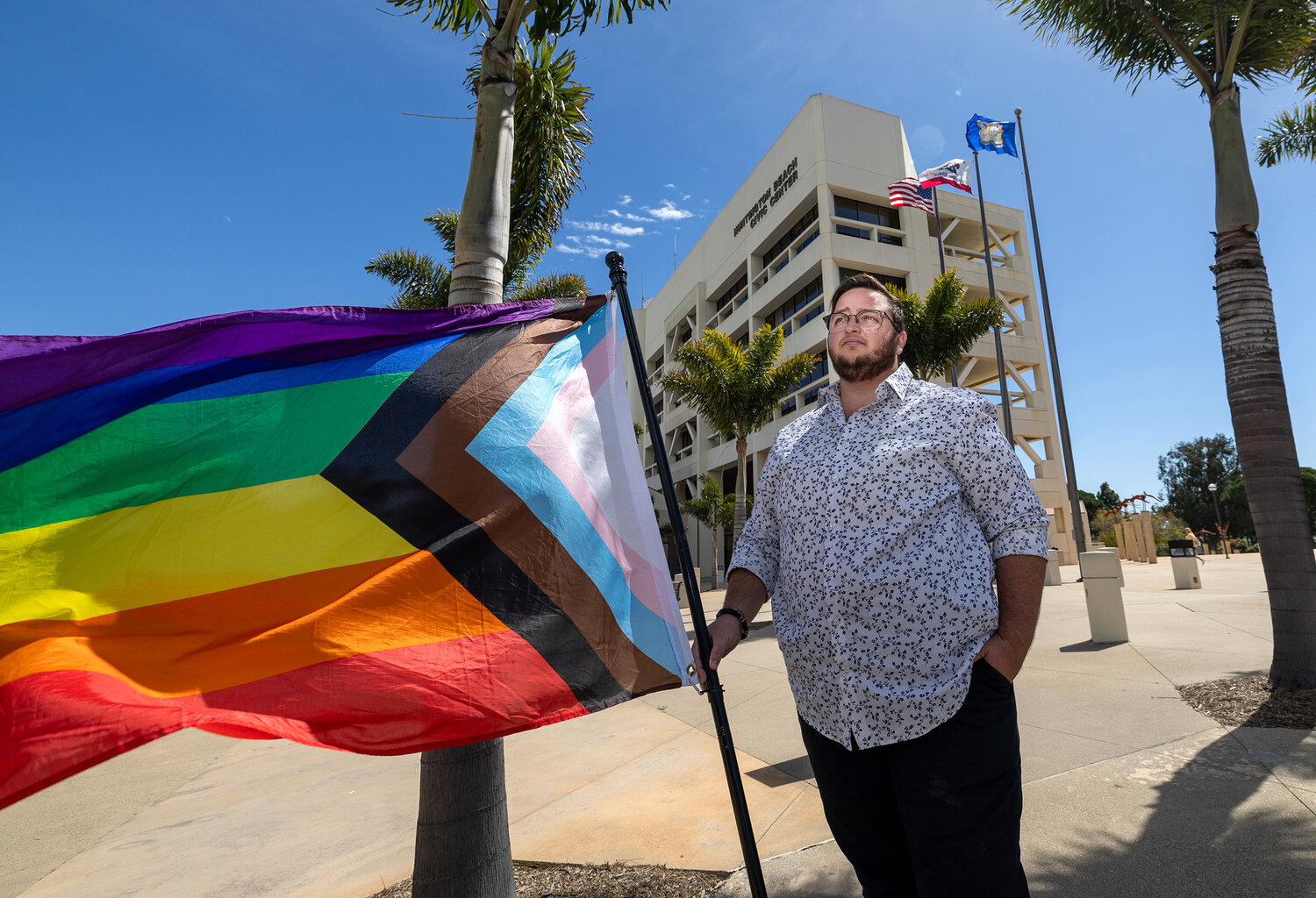 A person stands with a Pride flag outside Huntington Beach City Hall in California. The Pride flag has evolved into many designs over the decades since its introduction.