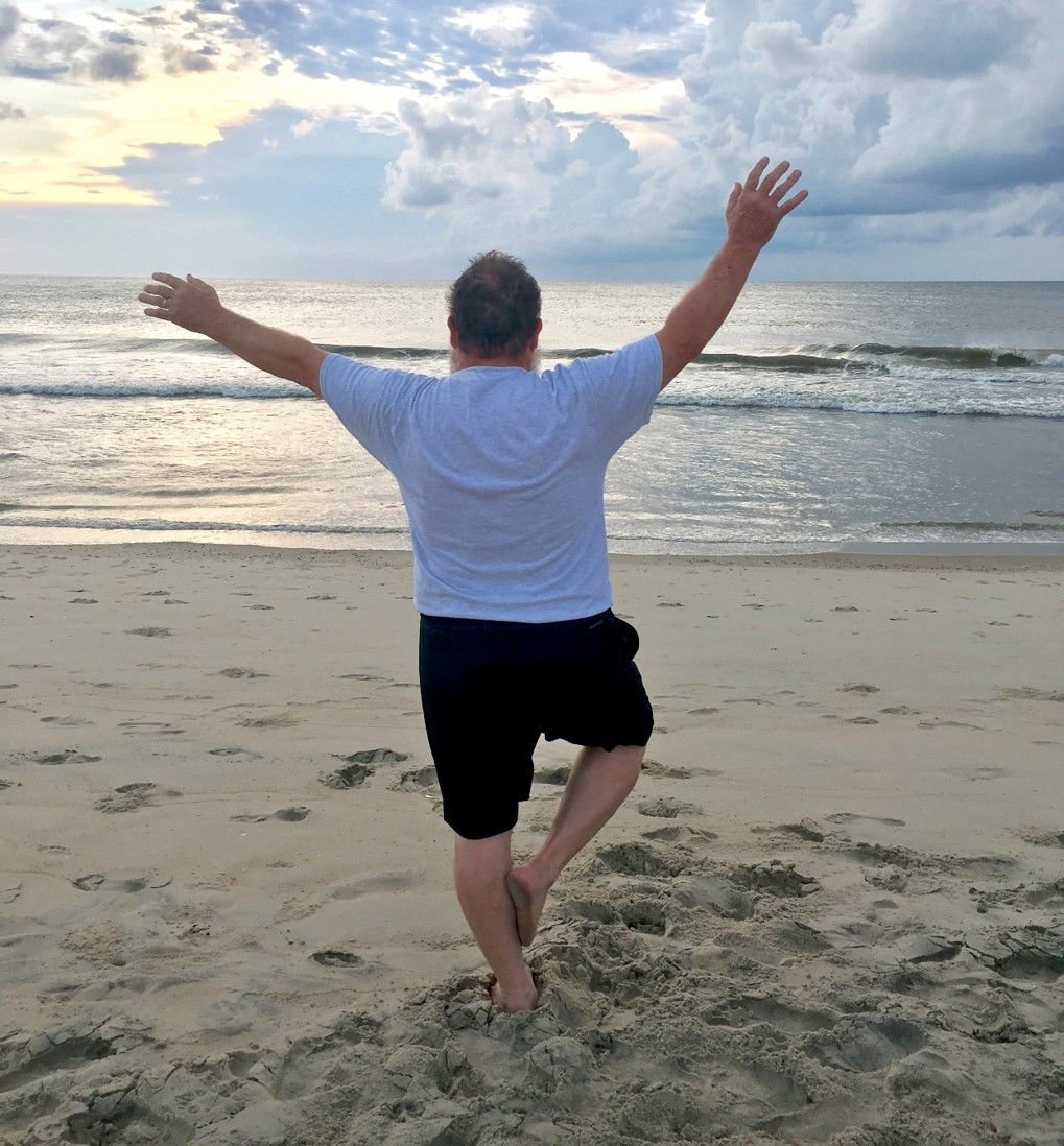 Rick Warner does a tree pose as the sun rises. He said the pose is much easier to do in the sand.