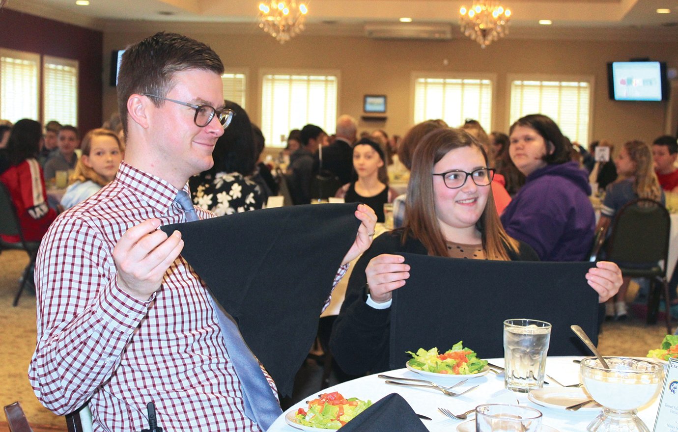 Craig Callahan, assistant principal at Crawfordsville Middle School, left, and sixth-grade students Aliyah Brost demonstrate proper napkin-folding etiquette during a training session Monday at the Crawfordsville Country Club.