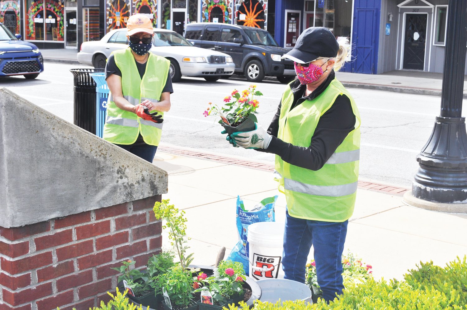 Belinda Kiger, right, inspects a flower before placing it in a planter as Marie Stocks puts on her gloves Monday at Marie Canine Plaza. Crawfordsville Main Street members planted flowers in the plaza after delivering hanging baskets for Crawfordsville Electric Light & Power employees to hang in the downtown area. The flowers were procured from Davidson Greenhouse & Nursery.