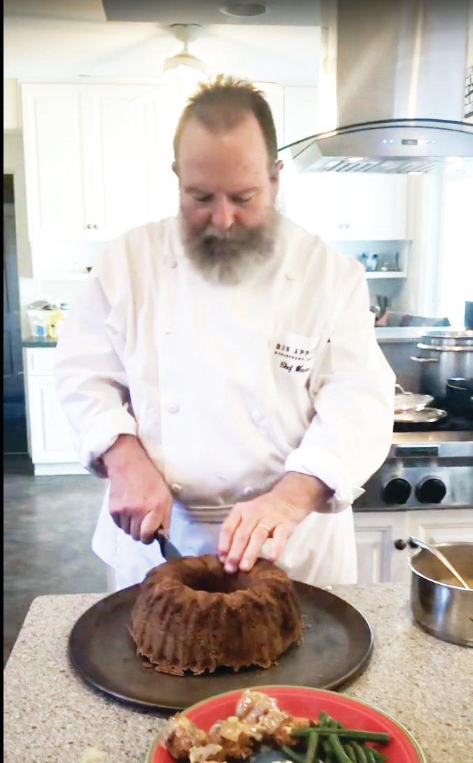 In this screenshot from a YouTube video, Rick Warner slices an apple spice cake. Bakers are following Warner's recipe to promote the Dr. Mary Ludwig Free Clinic.
