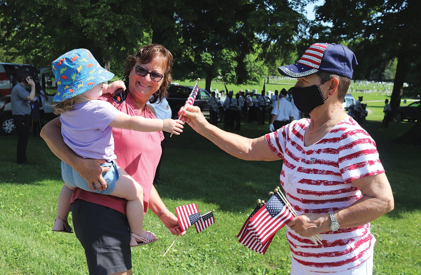 Carol Roberts, right, hands a miniature American flag to Angel Cooper and grandaughter Meadow Pitts during Memorial Day services at Oak Hill Cemetery on Monday.