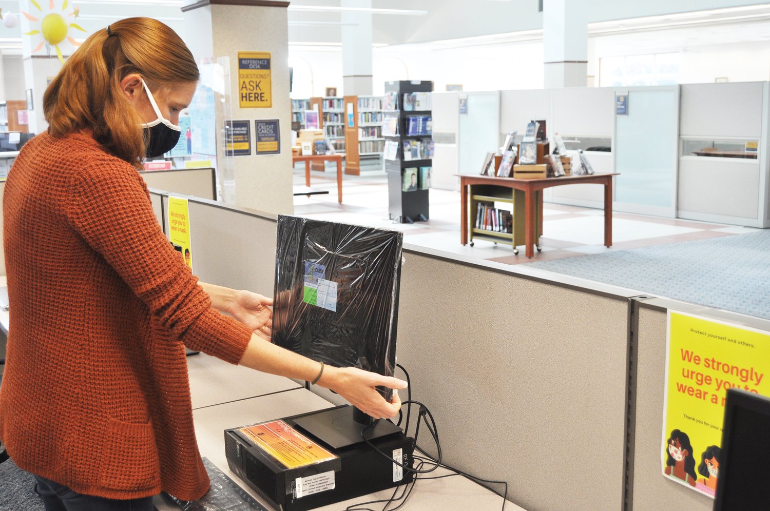 Megan Noggle adjusts a computer monitor after wrapping it with a plastic covering Wednesday at the Crawfordsville District Public Library. The library, which reopened Monday, strongly urges patrons to wear a mask and requires employees to cover their faces in public areas of the building.