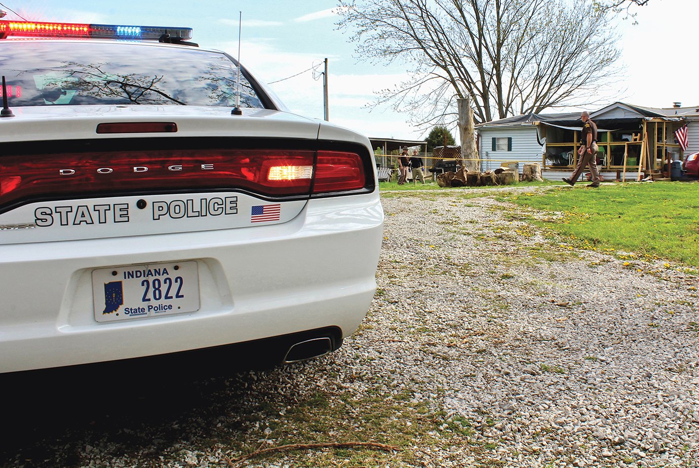An Indiana State Police squad car sits idle as officers from multiple agencies investigate a crime scene.