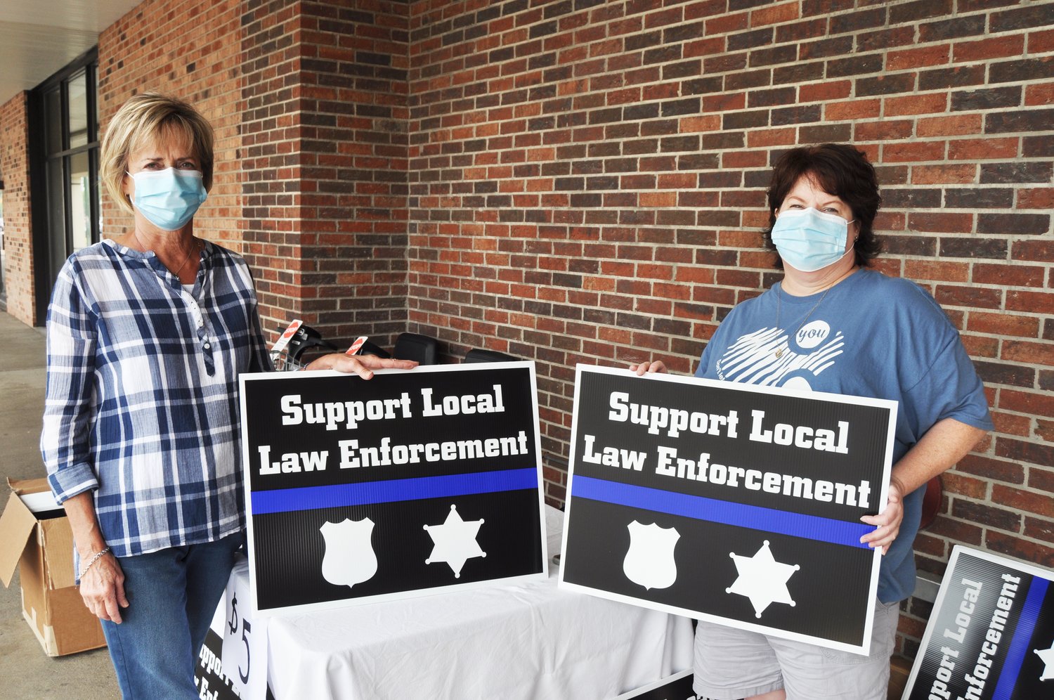 Bonnie Mills, left, and Mindy Byers hold signs they were selling supporting local police officers Saturday at Kroger. The project has received support from surrounding counties.