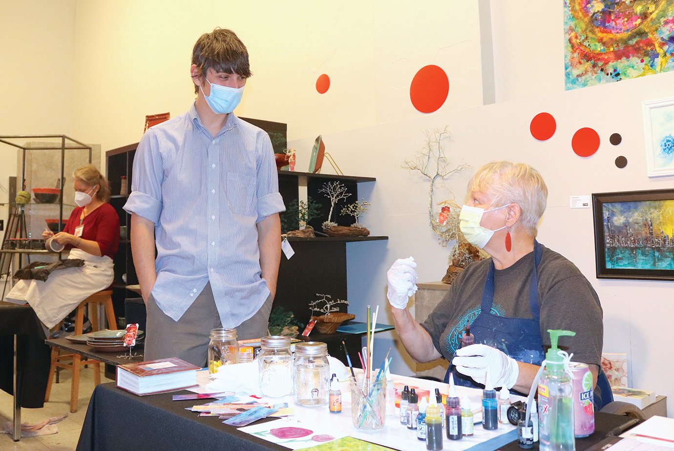 Member artist Ellie Dieckmeyer, right, demonstrates her alcohol-based ink medium Sunday at the Athens Arts Gallery to helper Jacob Ott.
