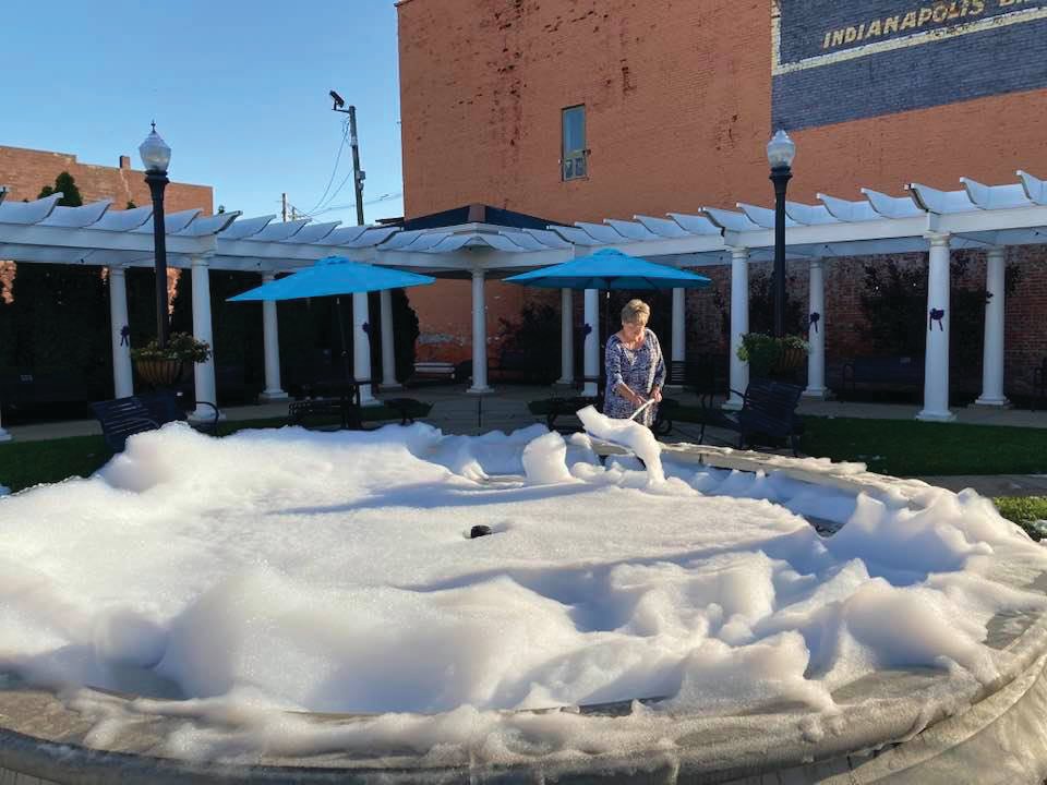 Sue Lucas, Crawfordsville Main Street program manager, scrapes foam out of the fountain at Marie Canine Plaza Friday. The fountain was soaped in the wee hours of the morning in an act of vandalism.