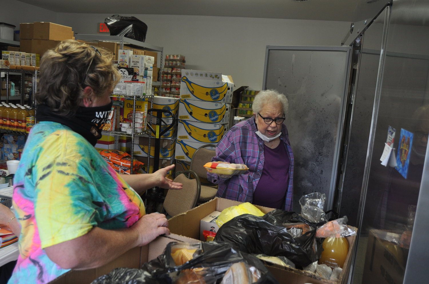 FISH Food Pantry manager Carol Spencer, right, hands a package of frozen chicken to volunteer Ellen Simpson on Friday. Area food pantries continue seeing high demand as the coronavirus pandemic wears on.
