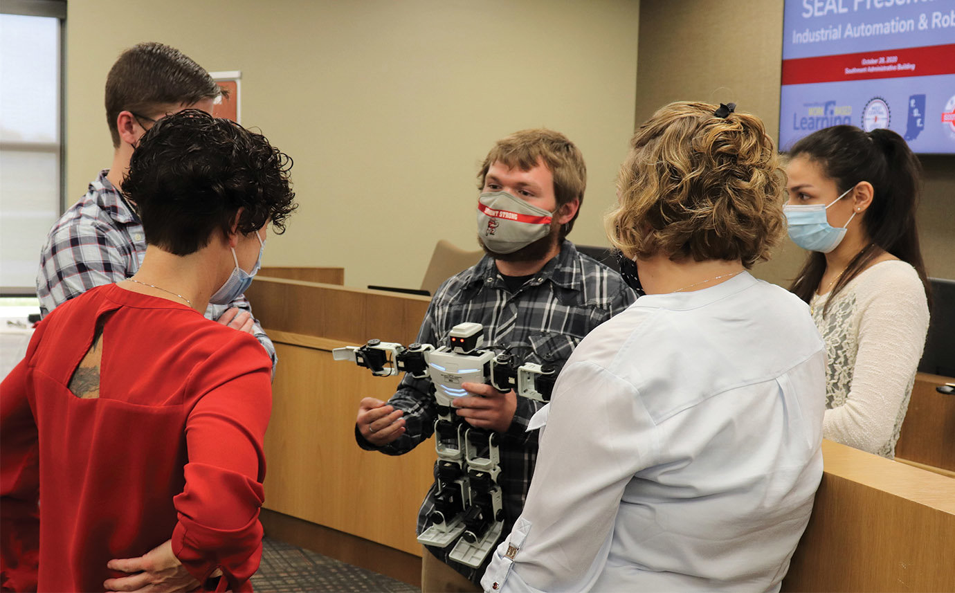 Southmont's Cole Endicott, center, and fellow students Clayton Moellers and Rose Perez explain the process of using an "ERIC" robot to Pace Dairy employee and Chamber President Tracy Mobley while course instructor Nicole Webb listens in.