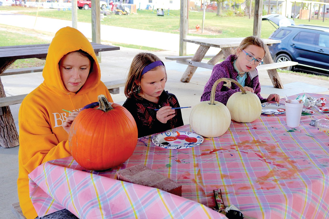 Rhyan Clemence, from left, joins Snyder sisters Millie, 8, and Taytum, 11, in the shelter at Linden's Bulldog Park on Thursday for pumpkin-painting fun.