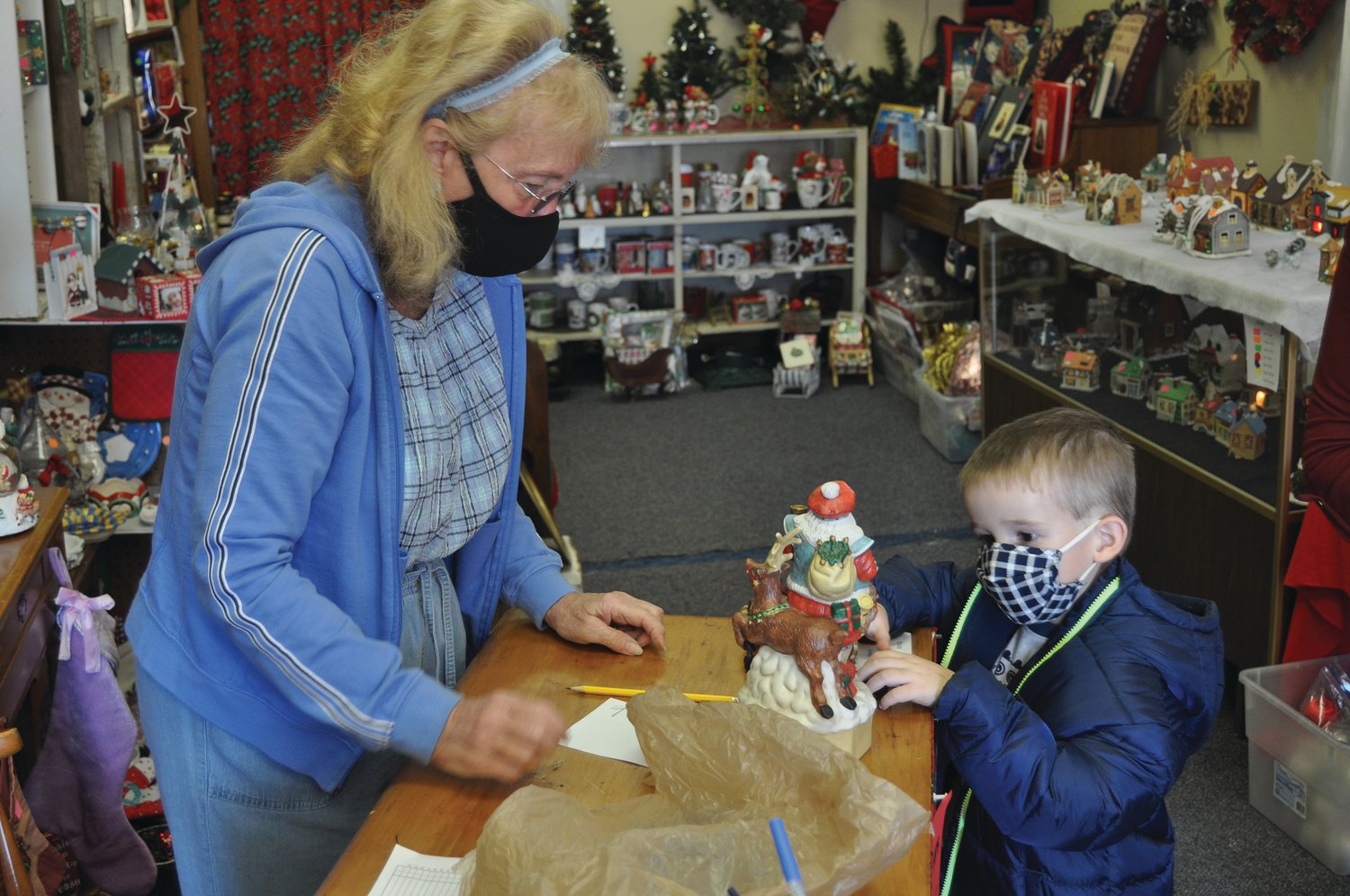 D.J. Alexander, 4, looks at a music box as Dee Isenberg waits to wrap it at the Christmas Shop on Friday. The shop raises money to provide food certificates to local families.