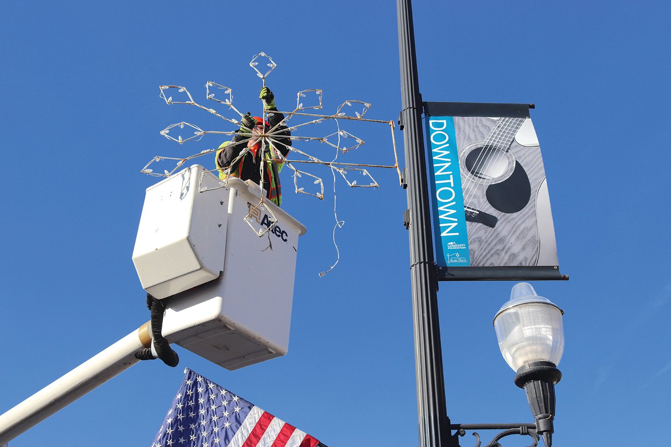 Another Christmas snowflake is affixed to a downtown light pole Tuesday by city employee Tom Edwards.