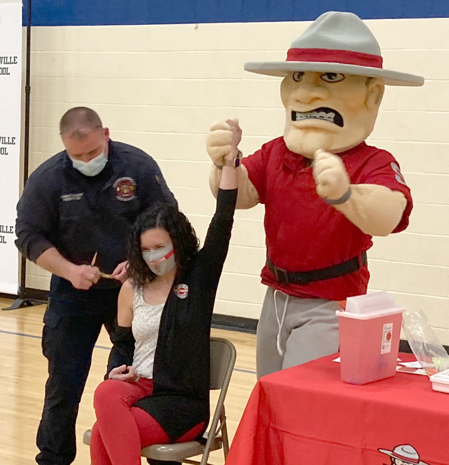Samantha Cotten, Southmont communications coordinator and college and career readiness coach,  celebrates with the Mountie Man as community paramedic Spencer Stevens finishes administering her COVID-19 vaccine Monday at Crawfordsville High School.