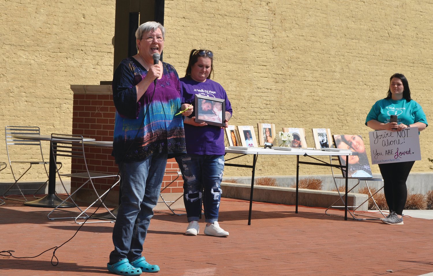 Jocele Harrison, first from left, speaks about her son Harold Barclay, who died by suicide, at the Walk of Hope at Pike Place Monday. Walk co-organizer Kaylie Edwards holds a photo of Barclay and his daughter, Lily, and Taylor Ratcliff holds a sign for suicide prevention awareness.