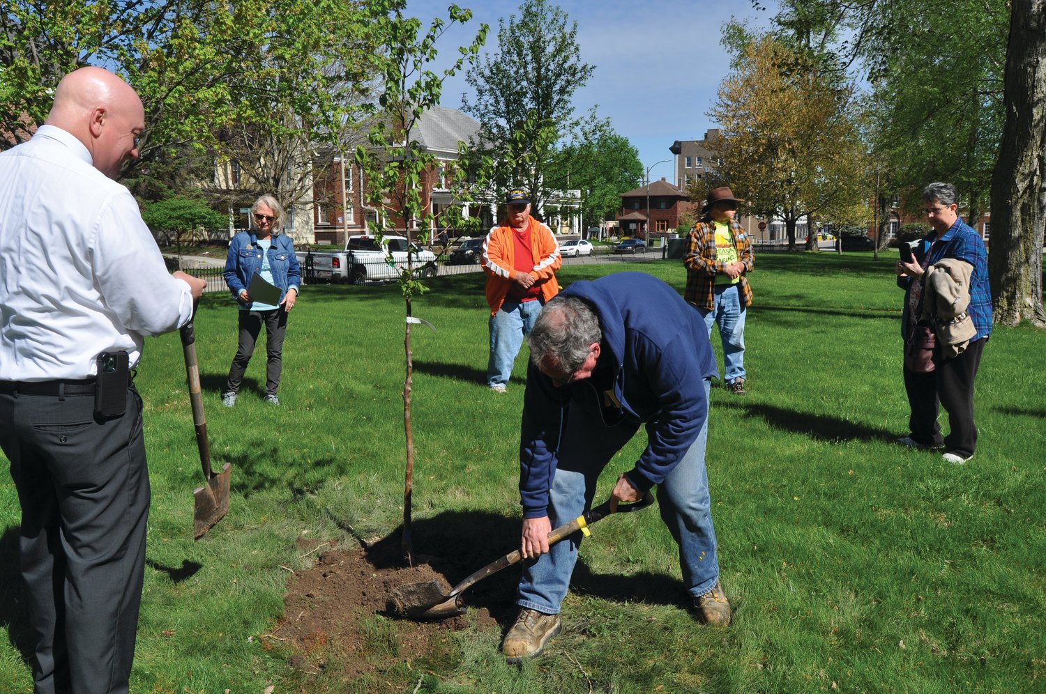 Jeff Bickel shovels dirt around an American Hornbeam tree planted in memory of his father, local naturalist Don Bickel, as dignitaries look on at the Lane Place Friday. Crawfordsville Main Street planted the tree and a Valley Forge elm on the museum grounds for Arbor Day.