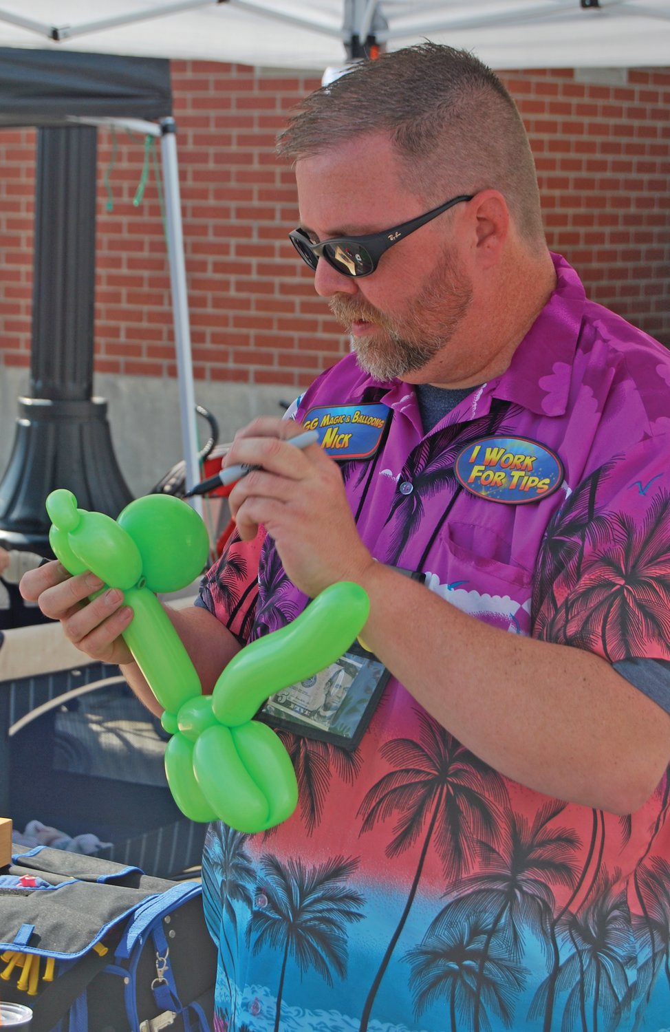 Nicholas Geigle draws eyes on a balloon animal at the Crawfordsville Farmers Market Saturday.