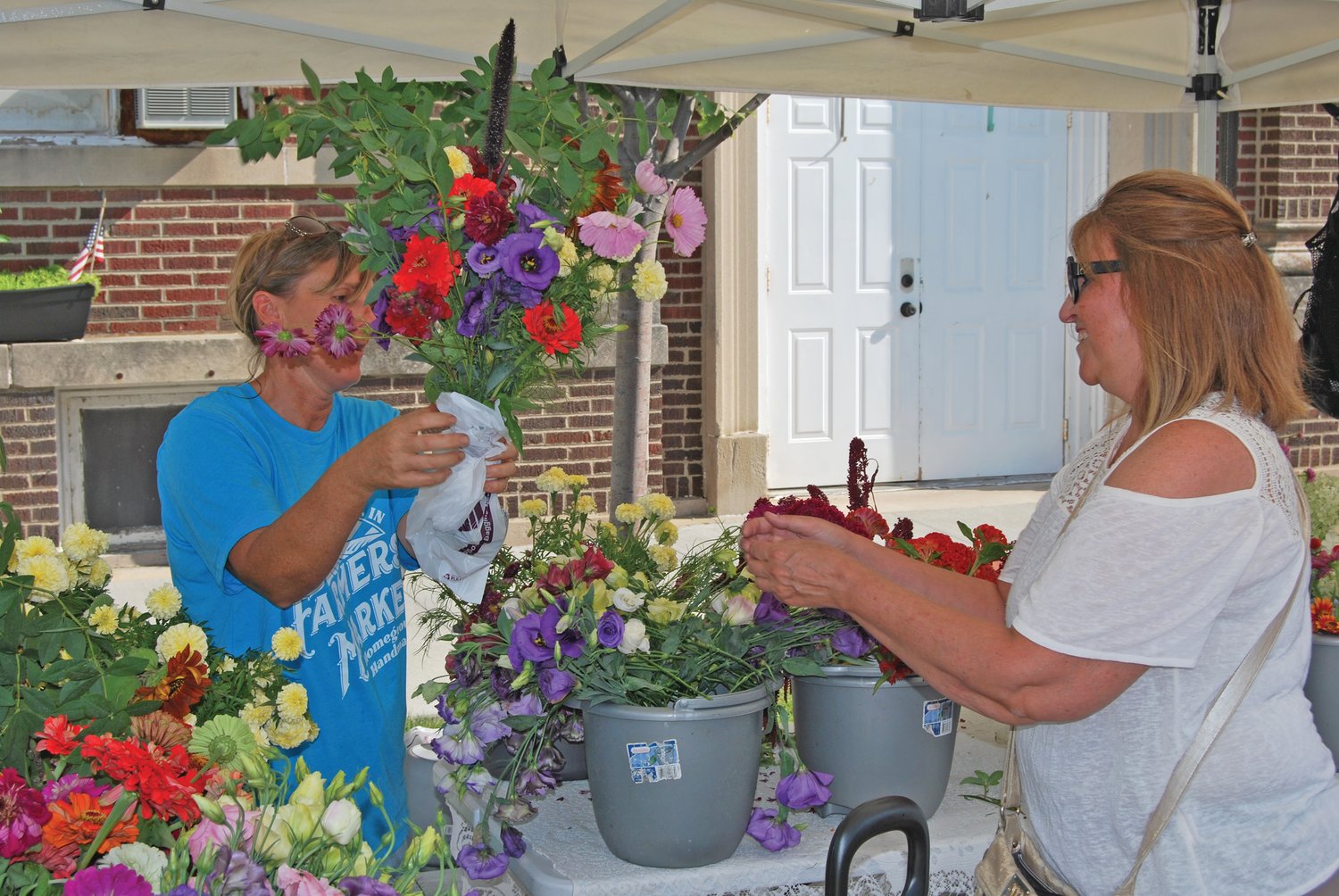 Jamie Smith of Fall Creek Farm hands a flower bouquet to Vickie Lingen at the Crawfordsville Farmers Market Saturday.