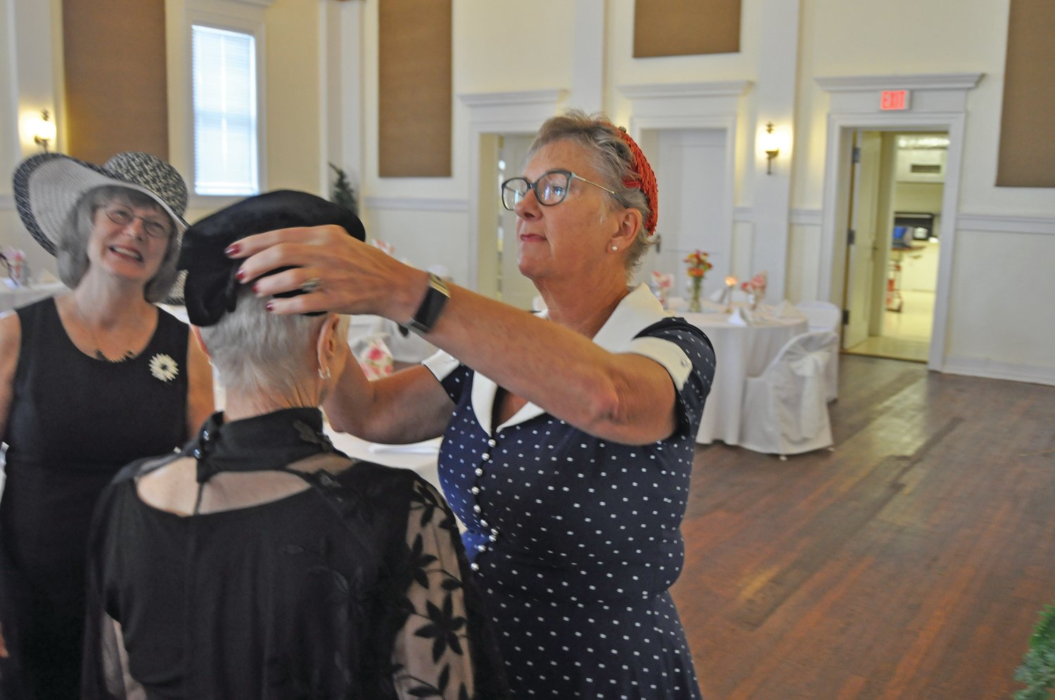 Terri Trinkle helps Ruth Hallett with her hat during a 100th anniversary of the Flower Lovers Garden Club at the Masonic Cornerstone Grand Hall and Event Center on Wednesday.
