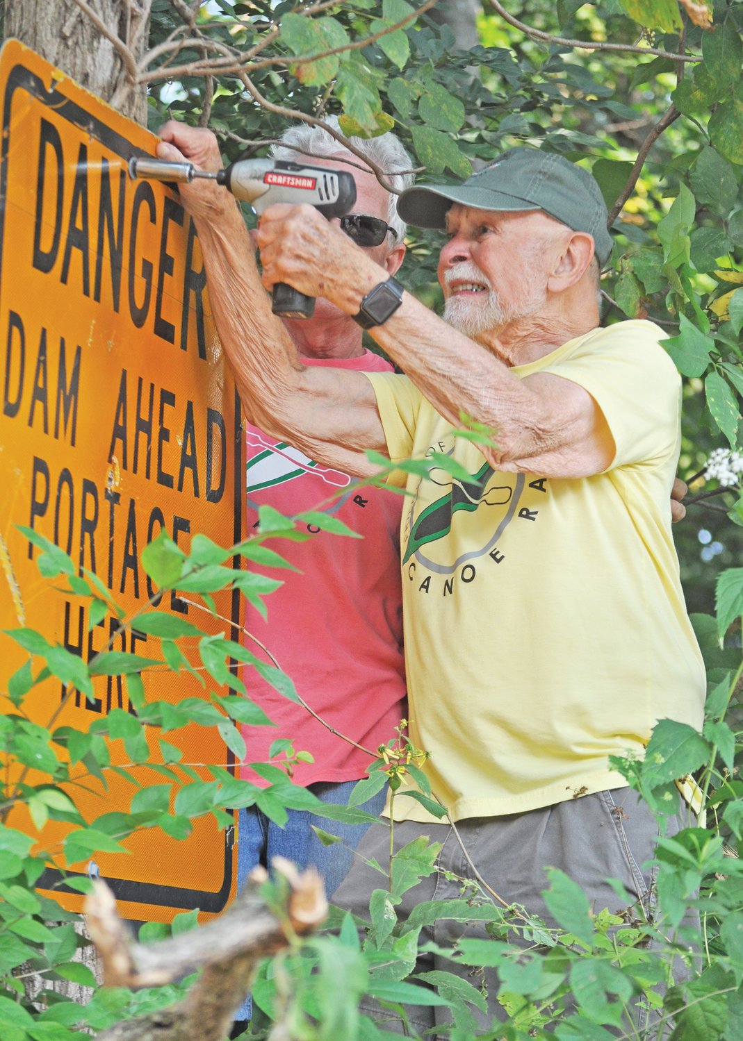 Austin Brooks, past president of Friends of Sugar Creek, works to remove a sign warning boaters of the Sugar Creek lowhead dam alongside current president Ed Fain on Monday. The dam was demolished last week.