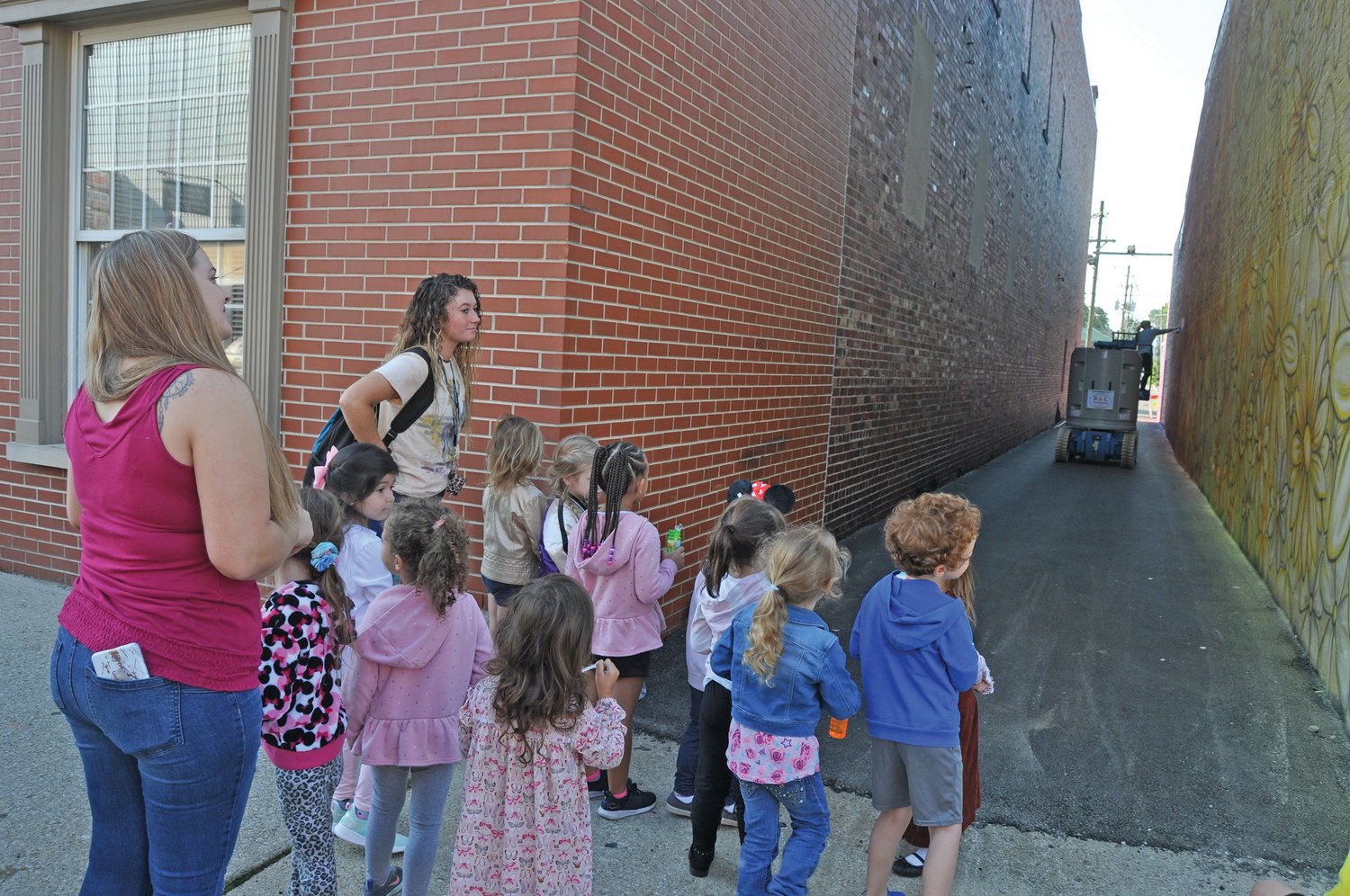 Children and staff from Rainbows & Rhymes Preschool and Child Care watch artist Jenna Morello work on the downtown alley mural on Wednesday.