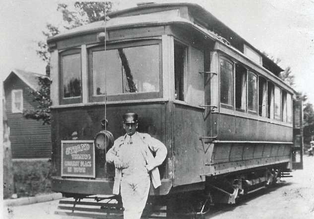 A man stands in front of a train or interurban car.