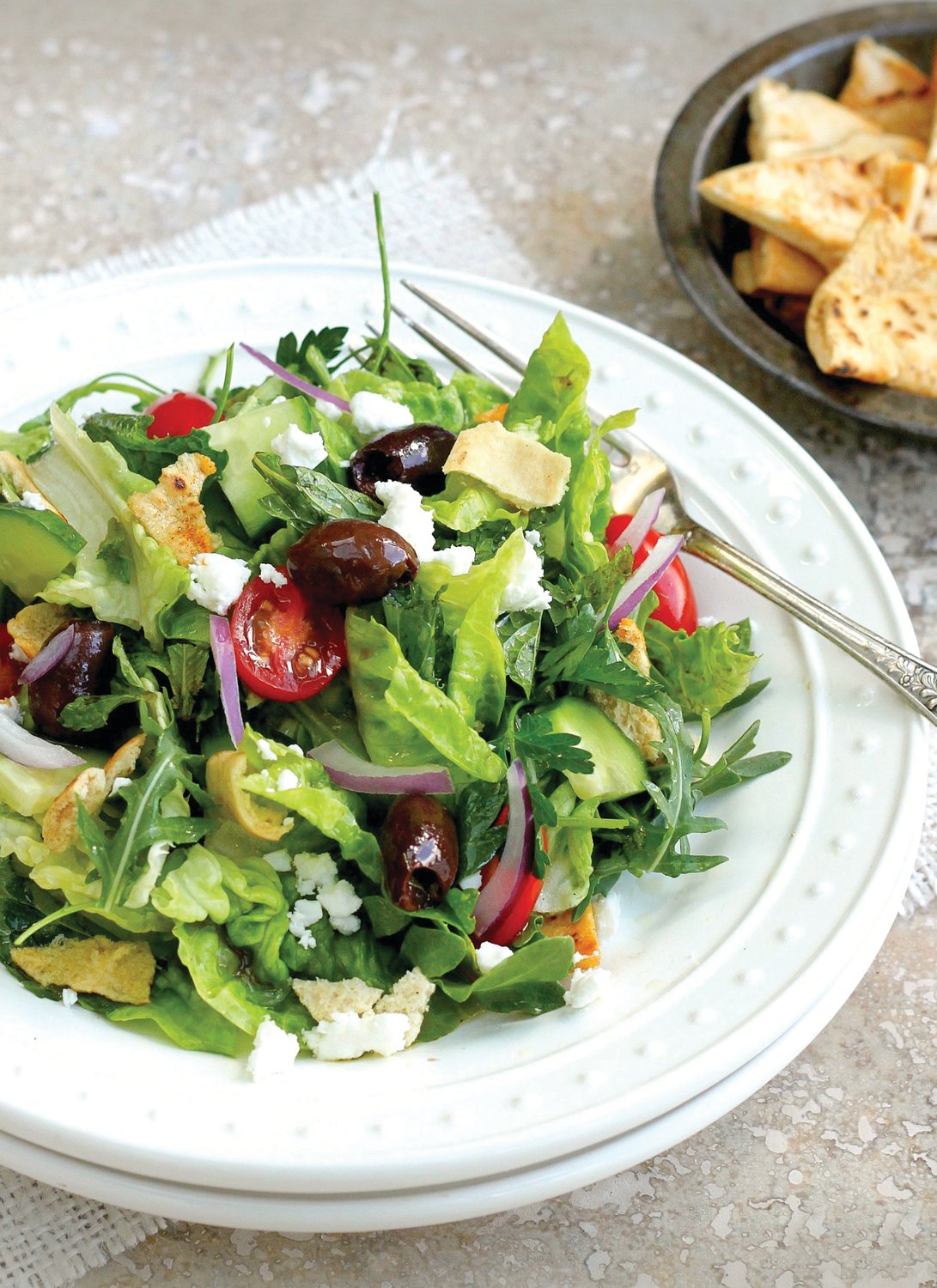 Fattoush is a garden salad and a bread salad at once, brimming with fresh greens and garden vegetables, studded with feta cheese and olives, and tumbled with shards of crispy pita bread.
