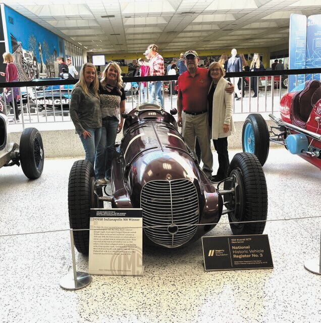From L-R: Miles’ adopted daughters” Jennifer Schneider and Jennifer Claborn stand with Randy Mikes and Patricia Miles  posing with Randy’s favorite car at the IMS museum.