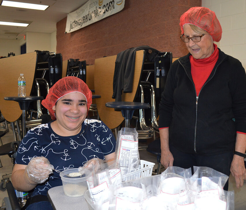 2023 Rise Against Hunger volunteer Angelie Cruz Maria completes a meal package. Looking on is Judy Hall of Millsboro's Grace United Methodist Church, which facilitated the event at Sussex Central High School.