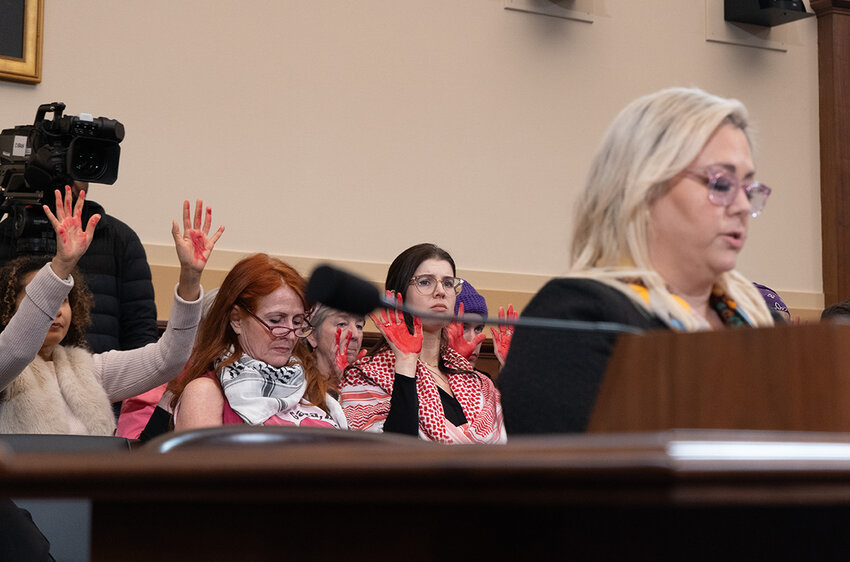 Code Pink protesters raise their paint-covered hands in a demonstration during a hearing of a subcommittee of the House of Representatives' Foreign Affairs Committee on Wednesday. The group is sitting behind Simone Ledeen, former deputy assistant defense secretary for the Middle East under President Donald Trump and now a senior fellow at the Strauss Center for International Security and Law.