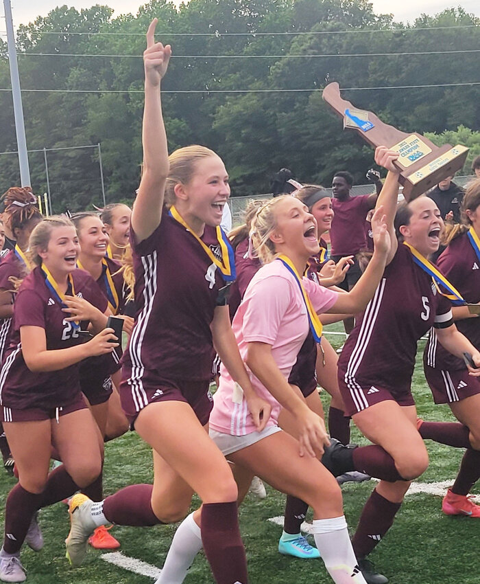 Appoquinimink High's Katie Donovan holds the state championship trophy while sprinting across the field.