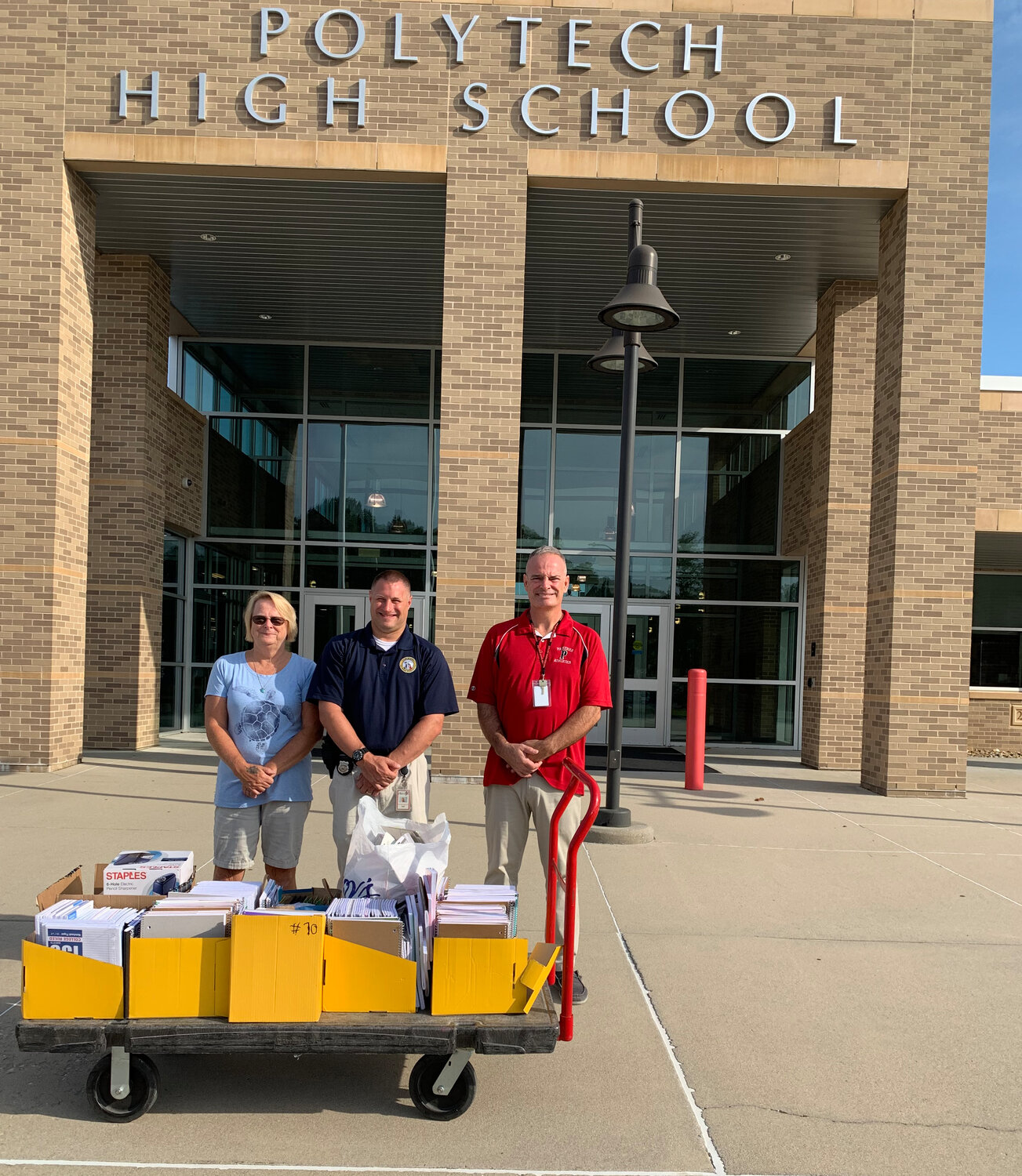 From left, Caring Hearts, Helping Hands director Nancy McCoury distributes school supplies to Polytech High School school resource officer Detective Nick Miller and custodian Drew Wooten.