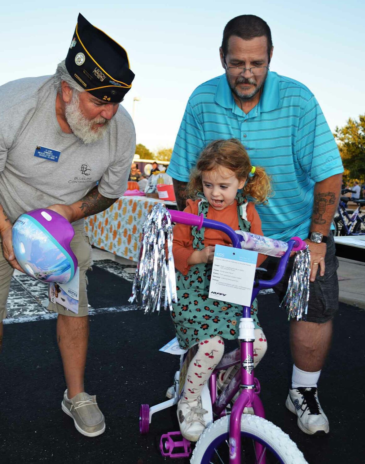 Dagsboro Mayor Brian Baull looks on as American Legion Post 24's Ty Remp presents a helmet to 4-year-old Callie Edwards as she sits on the bicycle she won during the 2022 Dagsboro Night Out.