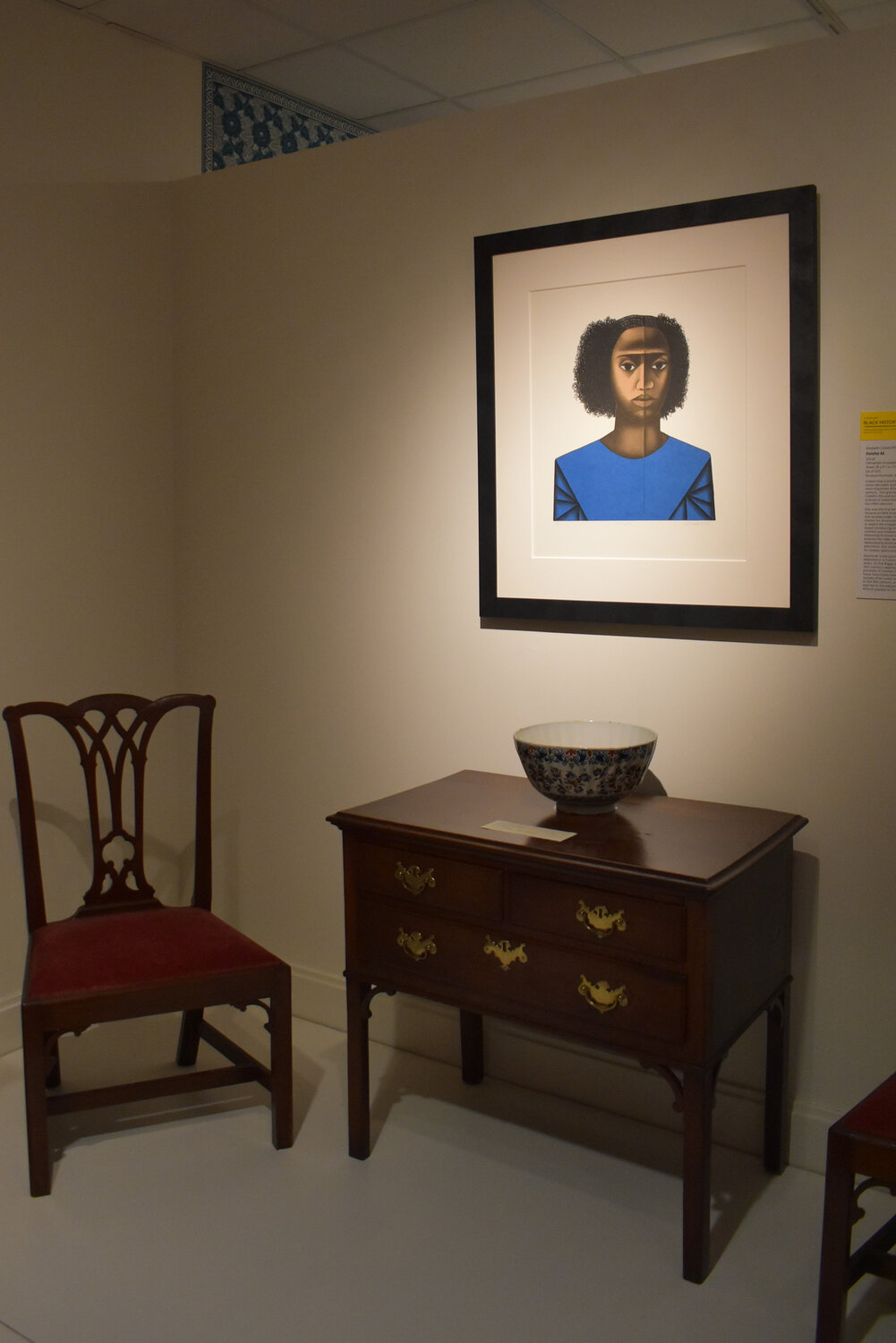 The 2008 lithograph “Keisha M.” by Elizabeth Catlett, with furniture at the Biggs Museum of American Art. An important African American artist, Catlett’s life (1915-2012) and art “were fueled by that legacy [of her ancestors’ enslavement]  and a sense of responsibility to those whose voices were too often silenced,” according to the Biggs. This image was intentionally hung in an 18th-century gallery near other portraits of women in blue—the demand for indigo dye spurred expansion of the slave trade.