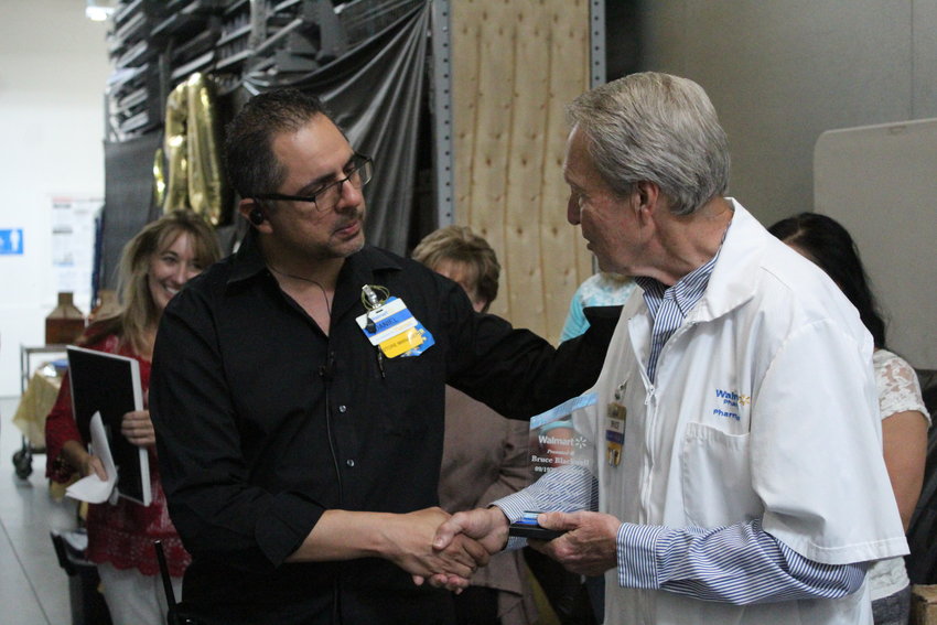 Gonzales Walmart store manager Daniel Trevino (left) shakes hands with Walmart&rsquo;s Pharmacist Manager Bruce Blackwell (right) as he congratulates him for 50 years of working with the company.