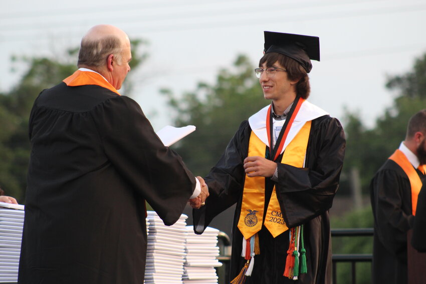 Valedictorian Cooper LaBuhn shakes hands with school board president Ross Hendershot, III and hand&rsquo;s LaBuhn his diploma.