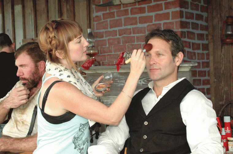 April Swartz applies some makeup to Tom Lagleder in preparation for a scene being shot at the Pioneer Village Living History Center in Gonzales, Texas. Greg Kelly is at the far left.