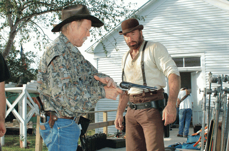 Doyle Culpepper (left) shows Greg Kelly the proper way to fan the hammer on a pistol for a shootout in the church (background) at the Pioneer Village Living History Center in Gonzales, Texas.