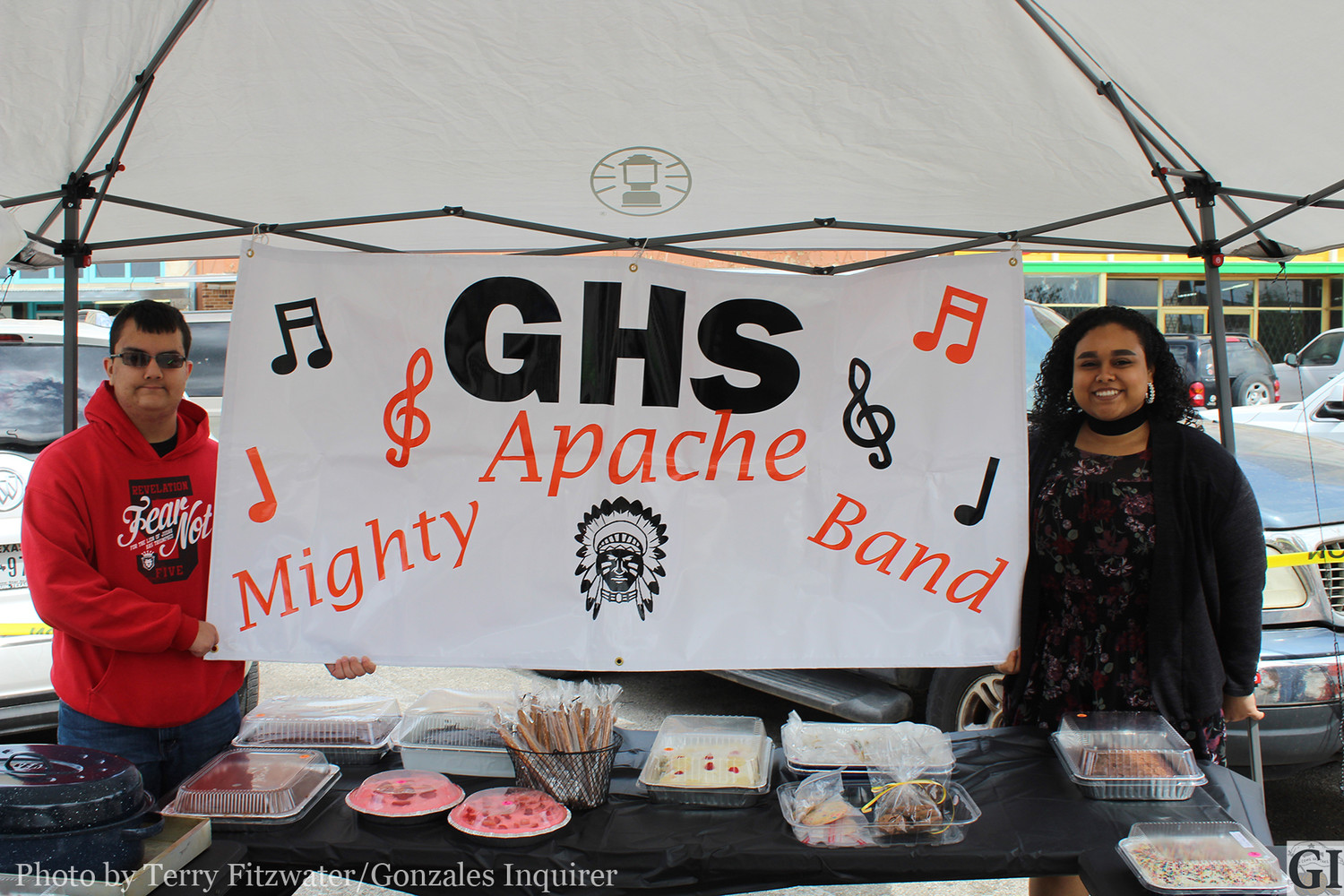 Joshua Kenning, left, a sophomore baritone player at Gonzales High holds the sign in the booth where band boosters were trying to raise money for new band uniforms by selling cakes, pies, pudding and other sweets. Also pictured is freshman Color Guard member Aaliyah Castro.