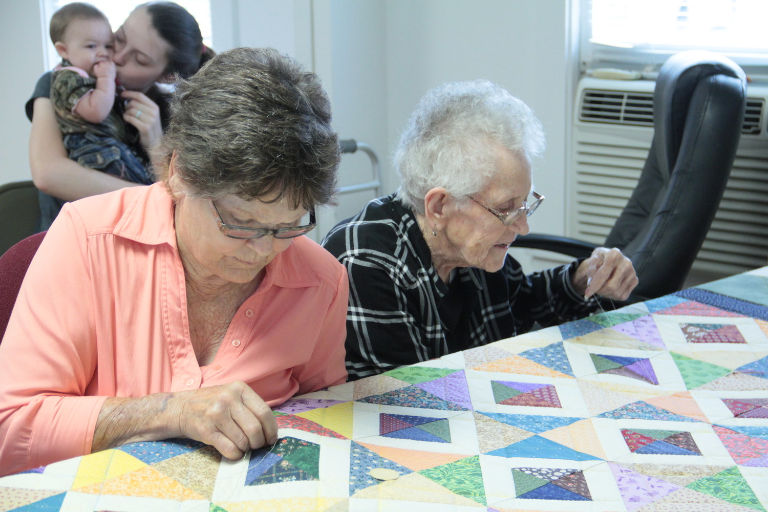 Margie Rice, left, and Janyce Littlefield, right, work on the quilt for the Leesville Country Fair auction. The work is the big-ticket item, fetching upwards of $2,000. Newest quilter-in-training Brooklyn looks on in interest from the back.