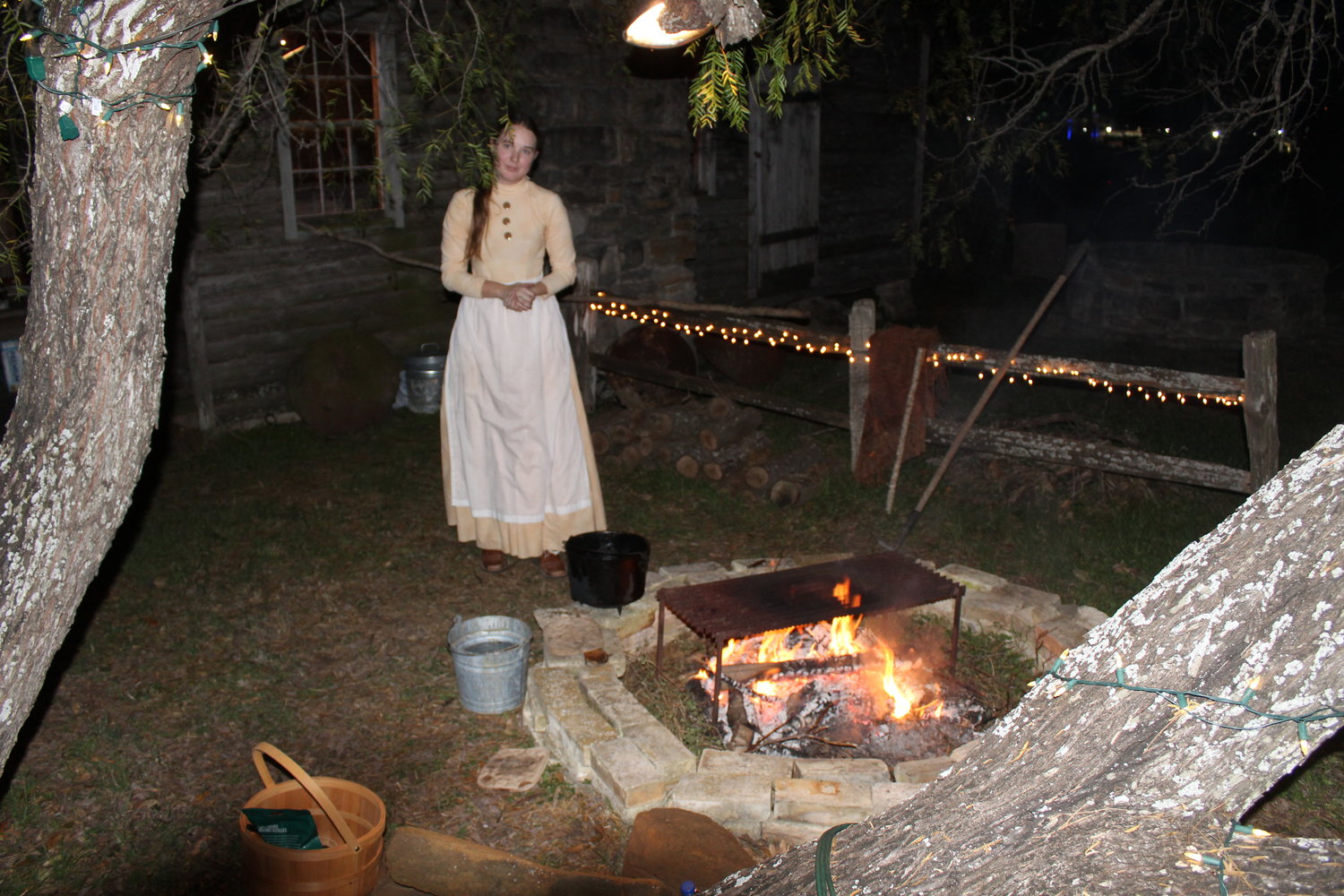 A costumed interpreter stokes the fire before visitors approached her building on Friday night.