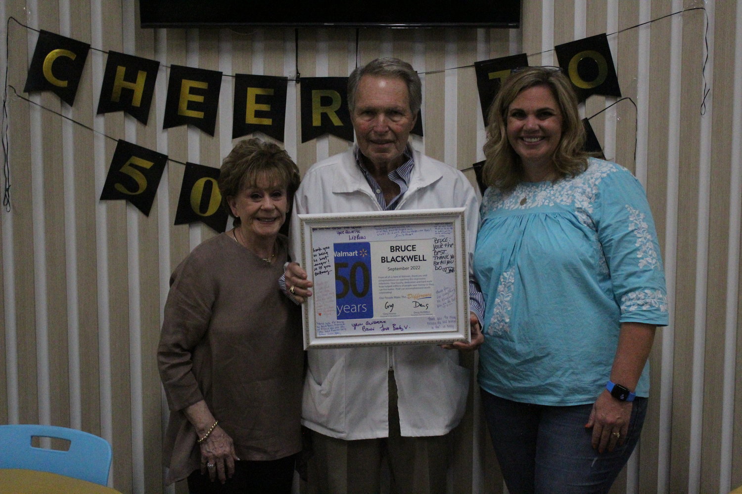 Gonzales’s Walmart Pharmacist Manager Bruce Blackwell (middle) with his wife, Wanette Blackwell (left) and daughter, Brittany DeBerry, as he holds his 50 year plaque.
