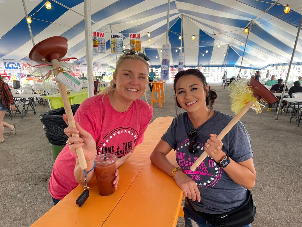 Come and Take It Celebration Committee Chairman Daisy Scheske Freeman, left, and Treasurer Naomi Brown hold decorated plungers in the beer tent during the 2023 event. The plungers are a familiar sight whenever the Shiner Hobo Band performs the traditional last Sunday set at the festival.