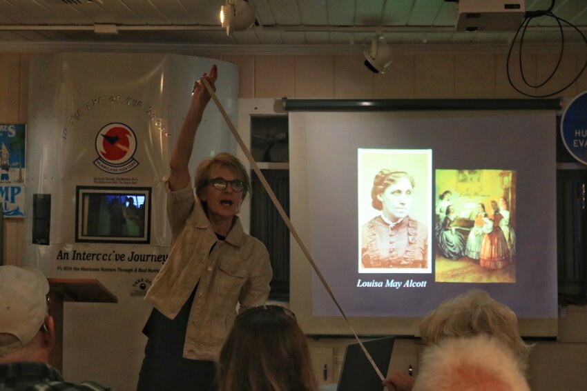 Dolores Hydock shows the length of hair Louisa May Alcott cut when she had typhoid fever by using a measuring tape and a participating audience member.