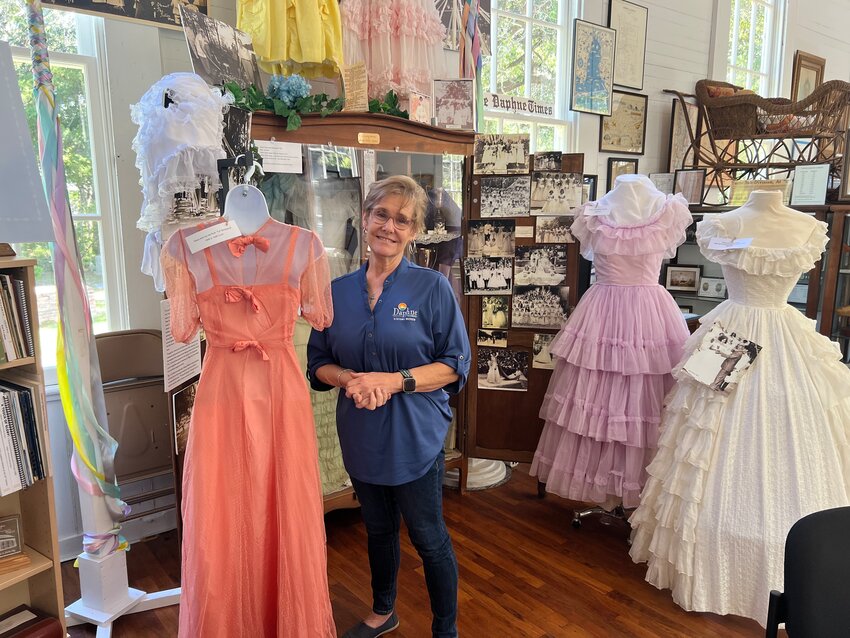 City of Daphne Museum Director Rachel Burt poses with May Day dresses worn by her aunt, mother and sister in Daphne May Day.