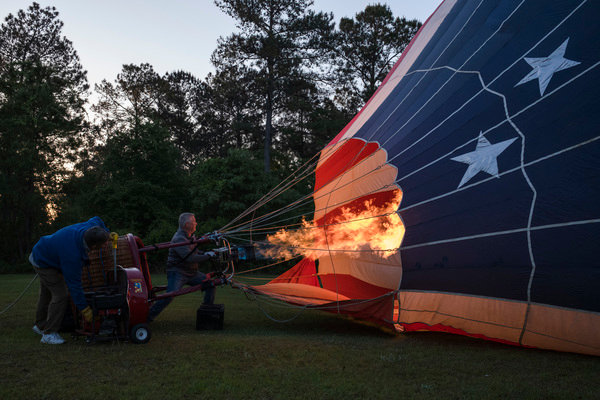 Gary Brossett (left), a hot air balloon pilot and crew member, directs a fan and while Rusty Miller uses a flame to inflate &ldquo;Stars &amp; Stripes&rdquo;, Miller&rsquo;s balloon, before a flight outside of Atmore.
